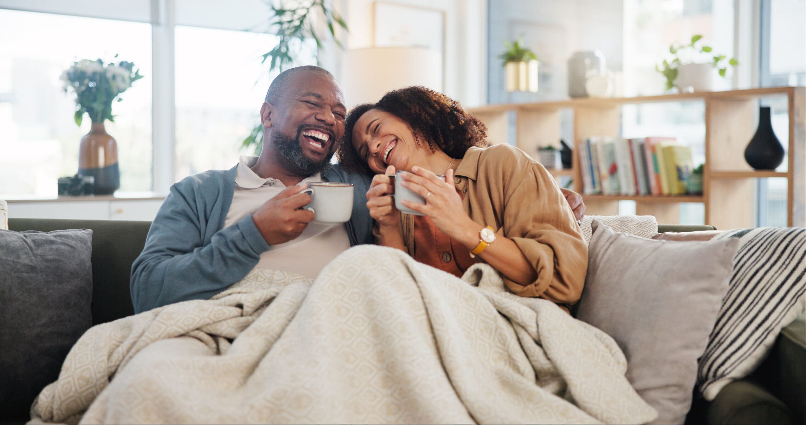 Laugh love and coffee with mature couple on sofa for bonding, marriage and romance. Happiness, calm and health with people drinking in living room of home for tea, communication and comfort together.