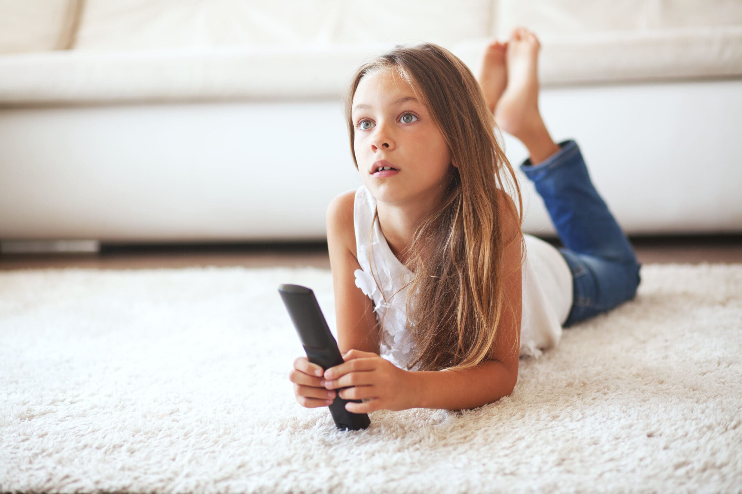 8 years old child watching tv laying down on a white carpet at home alone